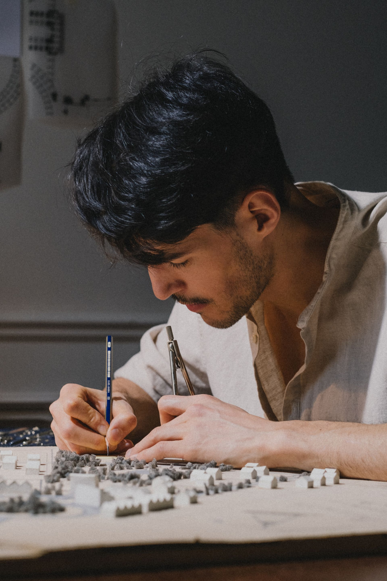 Architect at a drafting table, working a compass over a scale model of a residential plan