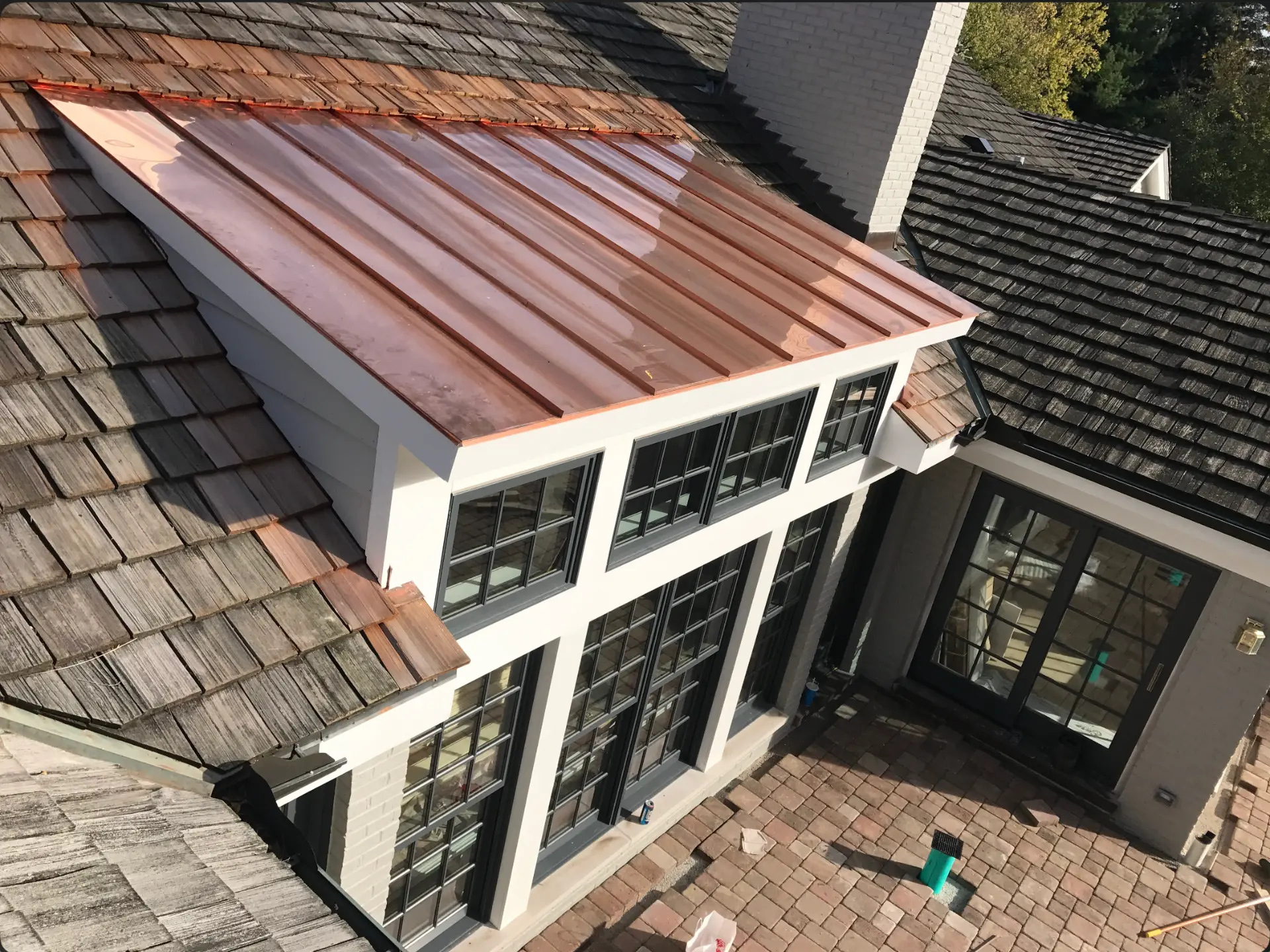 Addition exterior with a standing-seam copper roof, dark divided-lite windows and white trim above a brick paver patio
