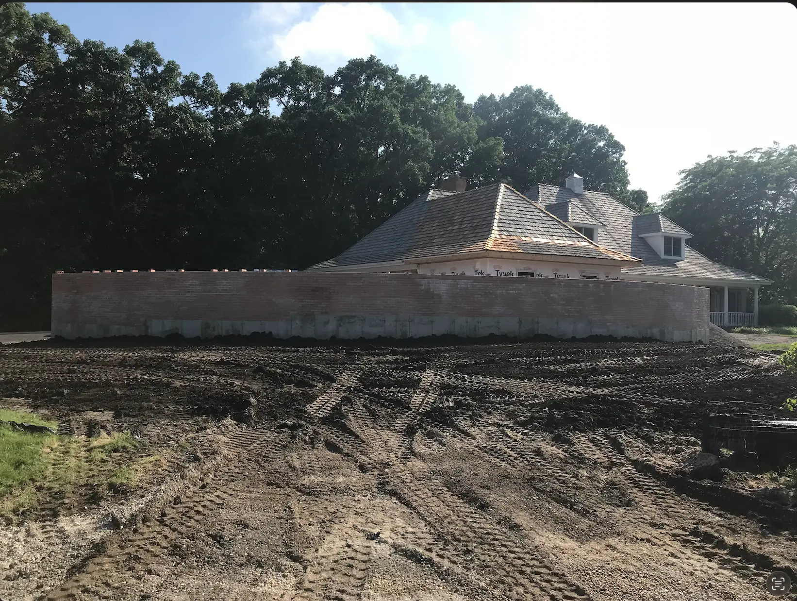 Home under construction with a brick wall and muddy unfinished lot